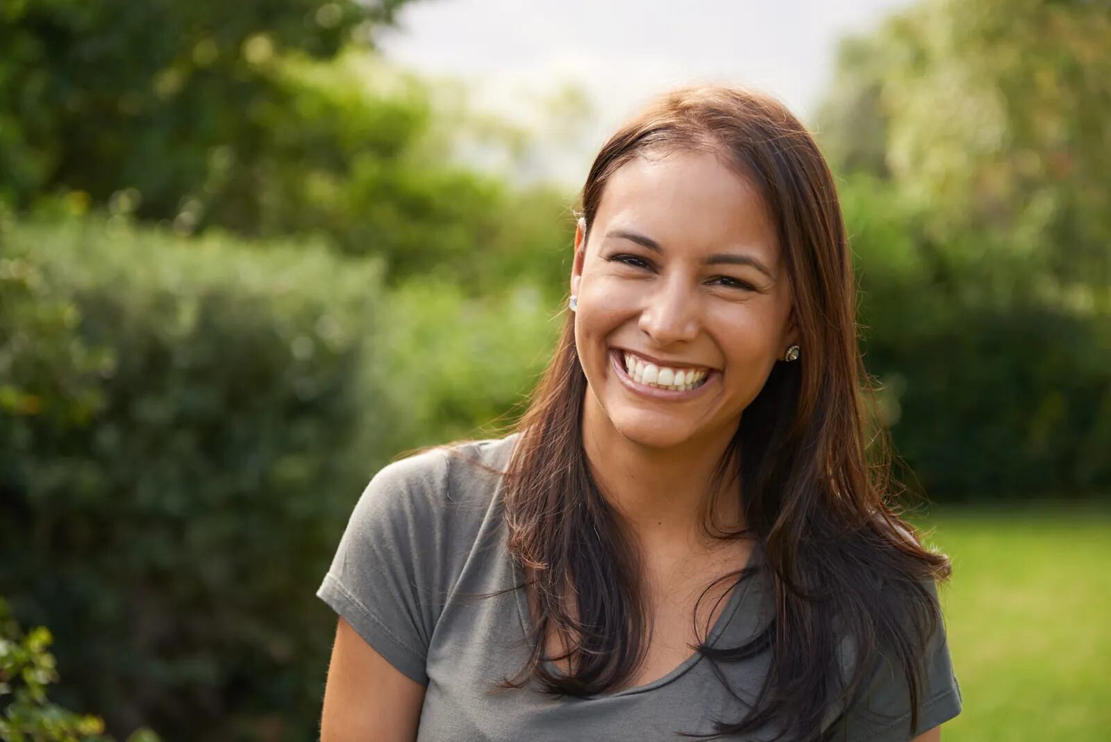 A woman with long dark hair smiling broadly in a garden