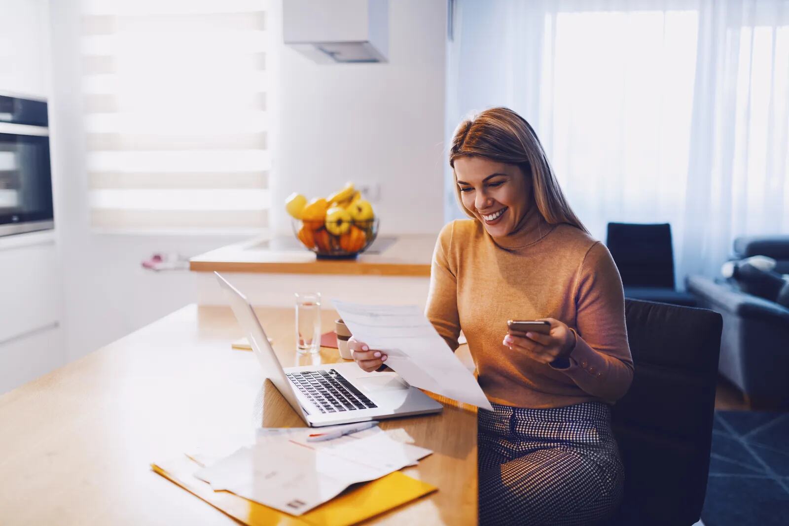 A woman smiling as she sorts her paperwork at the kitchen table